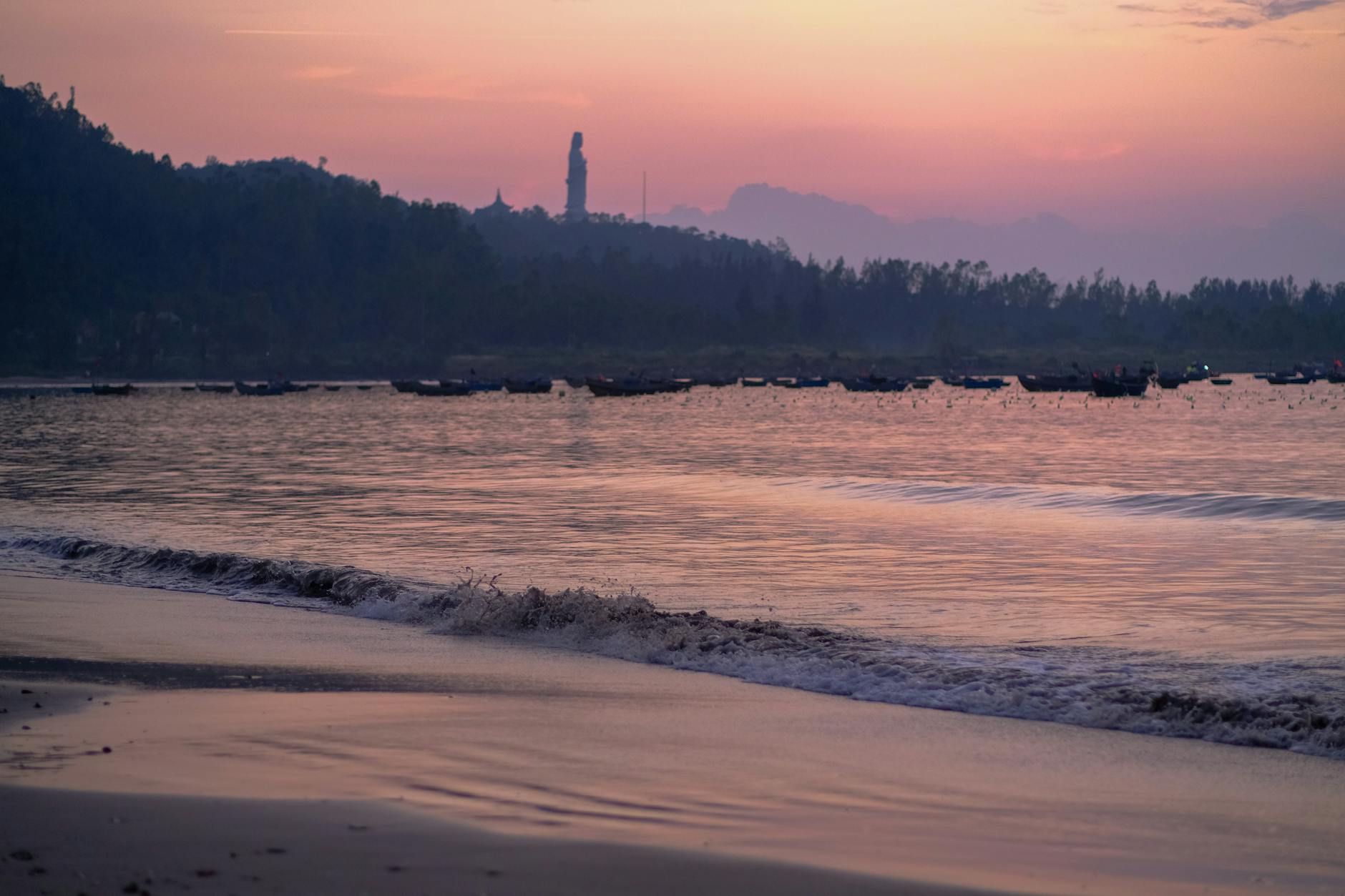 Peaceful sunrise view at My Khe Beach, Da Nang, with boats and mountains.