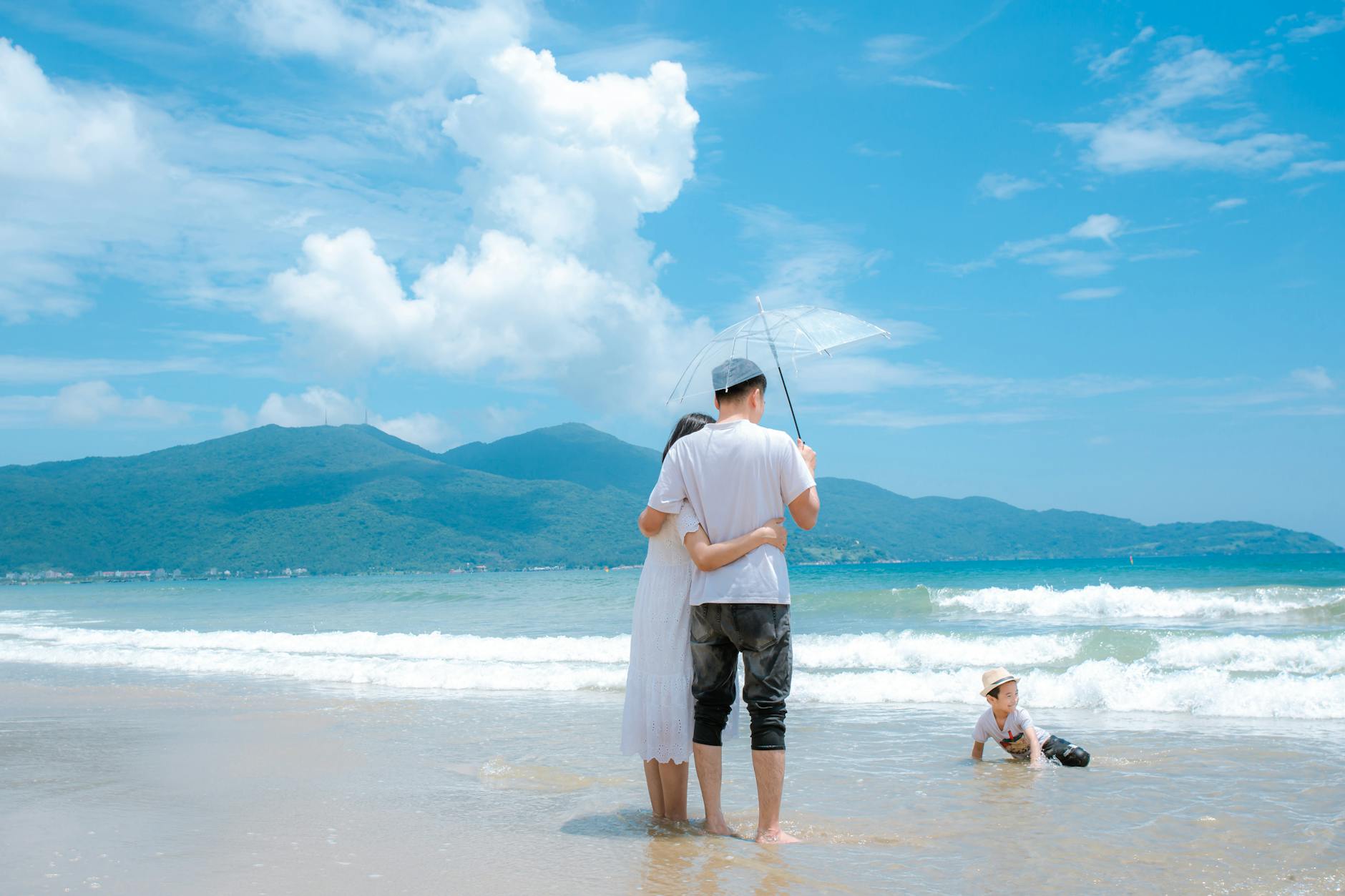 A joyful family enjoys the sunny day at Da Nang Beach, Vietnam, with mountains in the background.