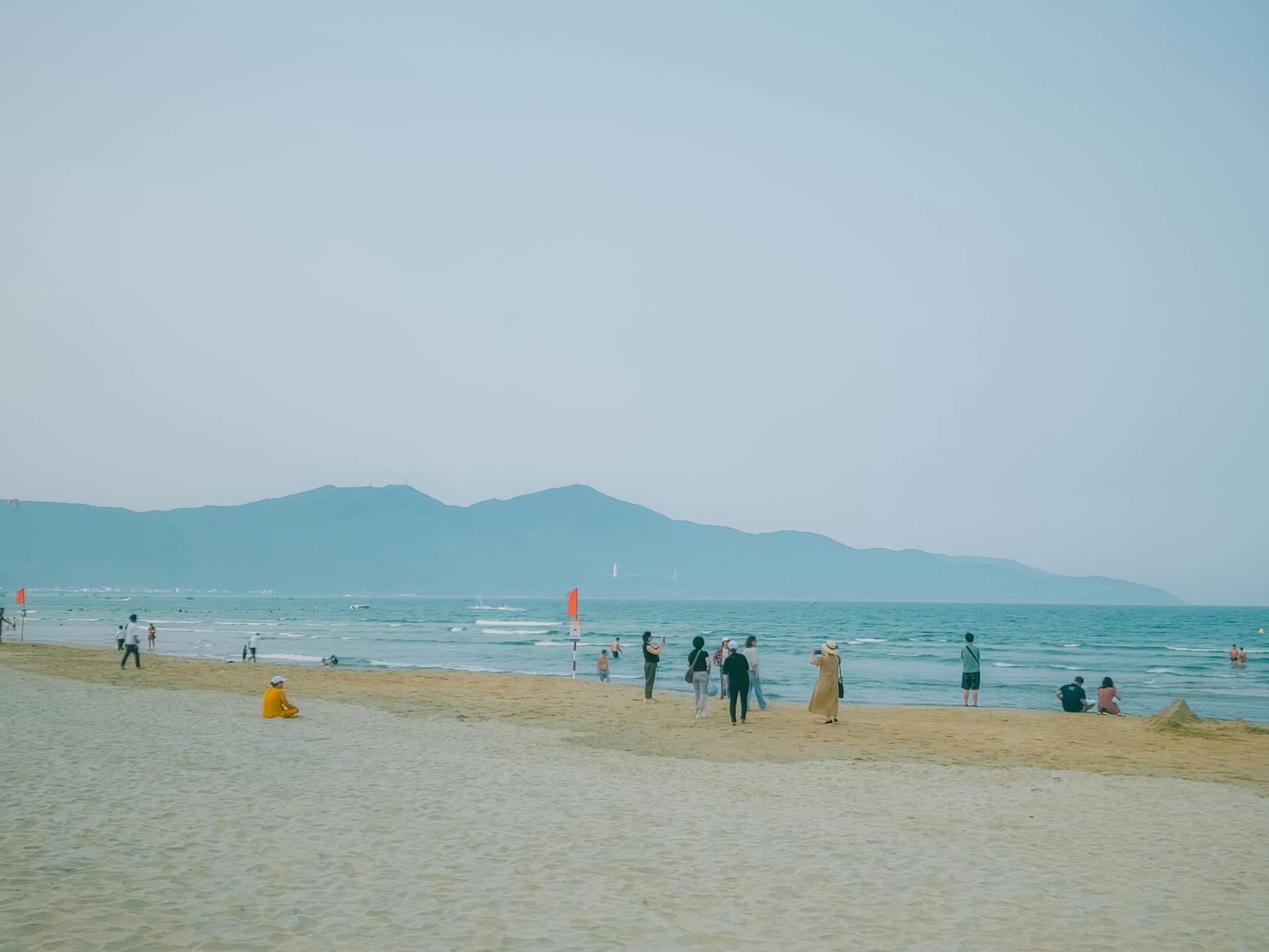 A serene beach in Vietnam with visitors enjoying the coastal scenery and distant mountains.