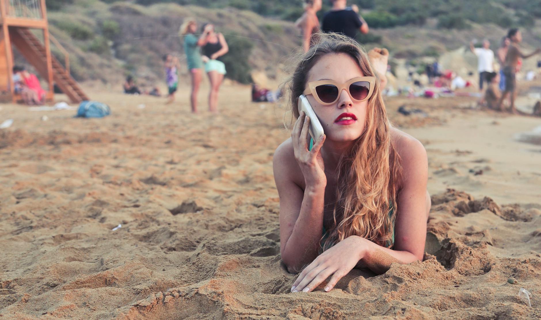 A woman with sunglasses relaxes on Mgarr Beach in Malta, talking on her smartphone.