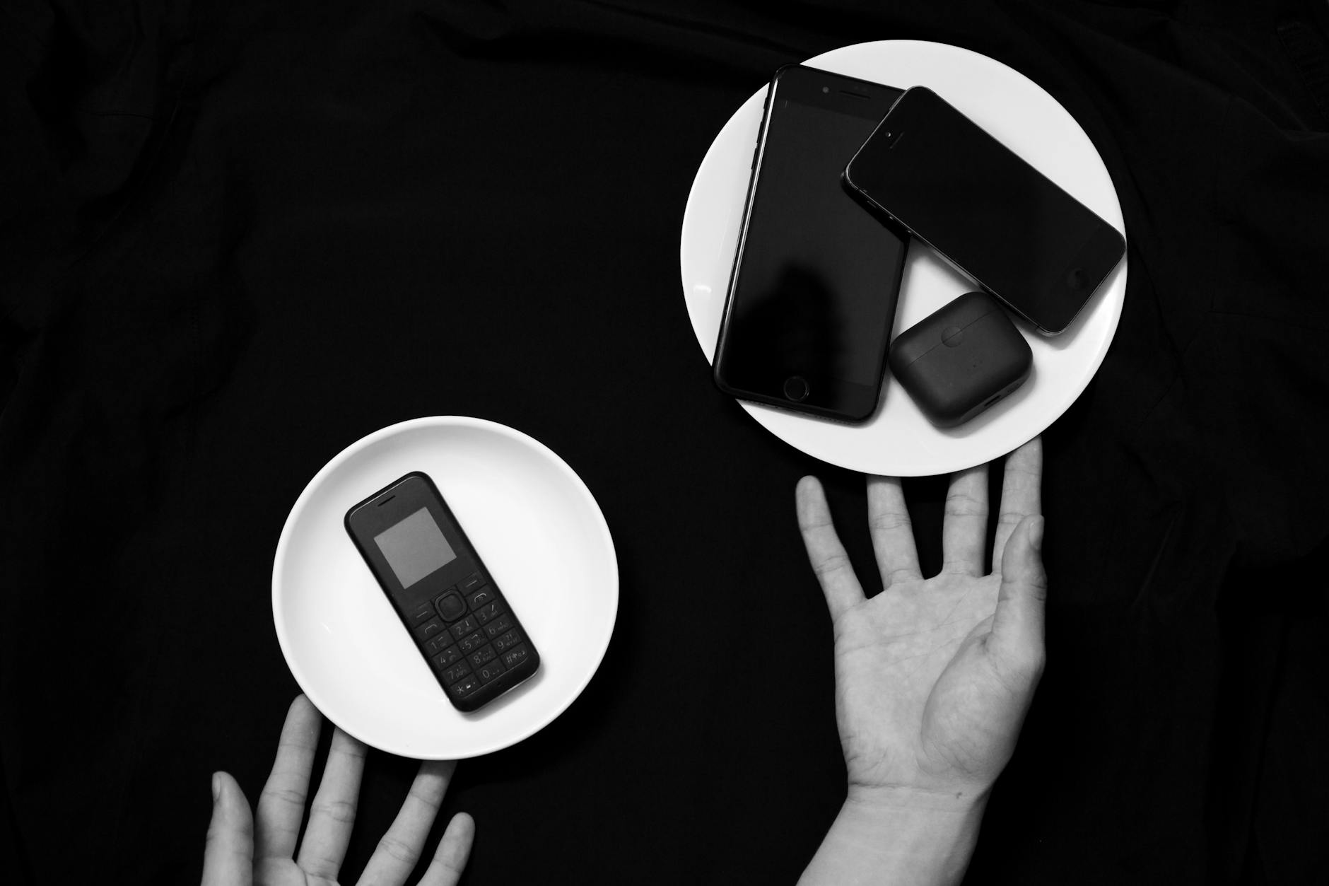 Contrasting old and new phones on plates in a minimalist black and white setup.