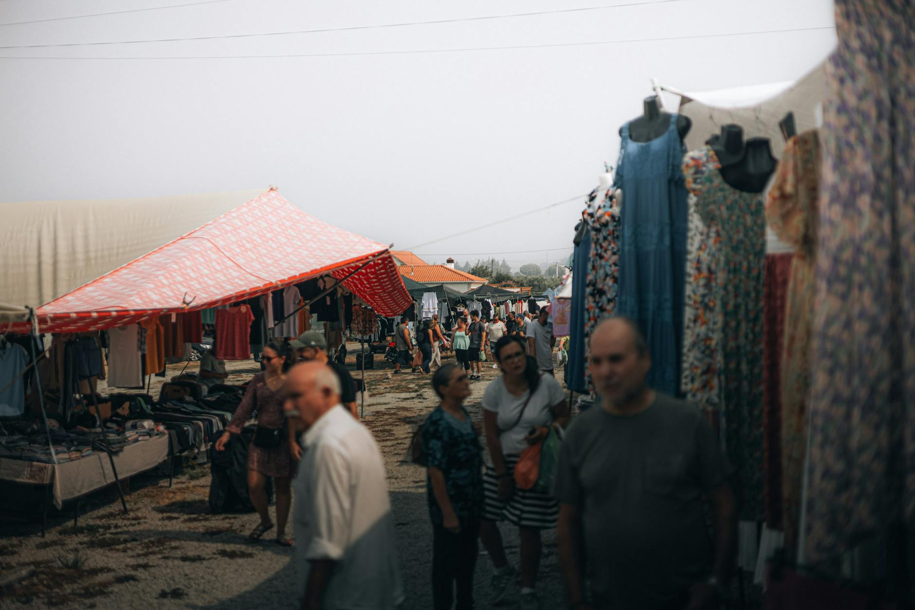 People explore a bustling outdoor market with colorful tents and clothing displays.
