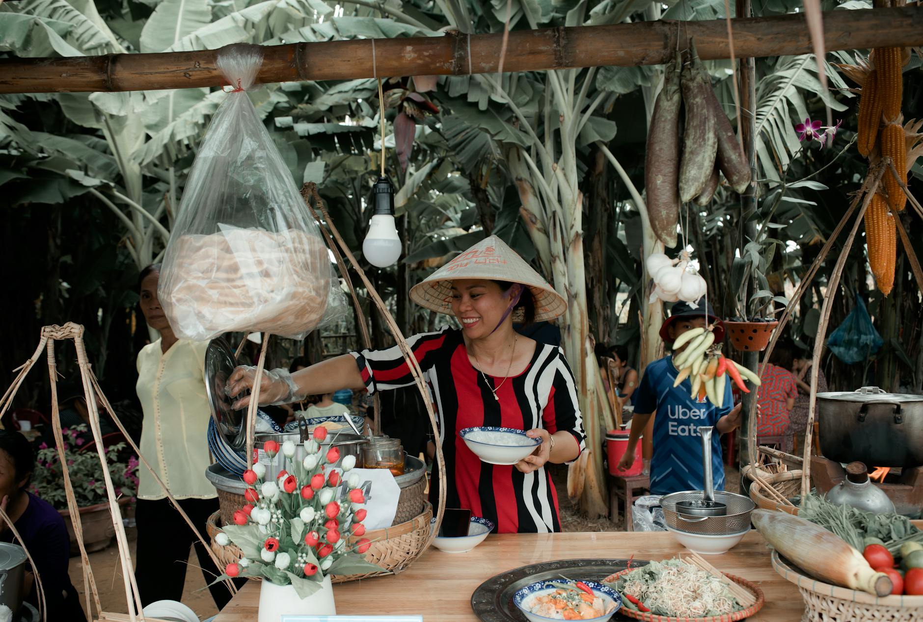 Asian woman vendor serving food in a vibrant outdoor market with tropical surroundings.