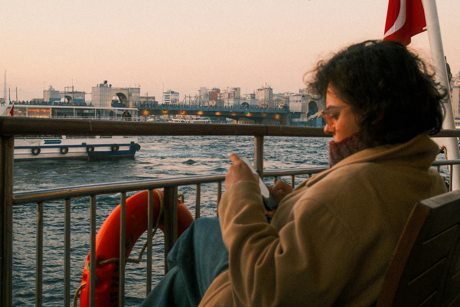 A woman enjoys a peaceful ferry ride on Istanbul's waters, with the city's skyline in the background.