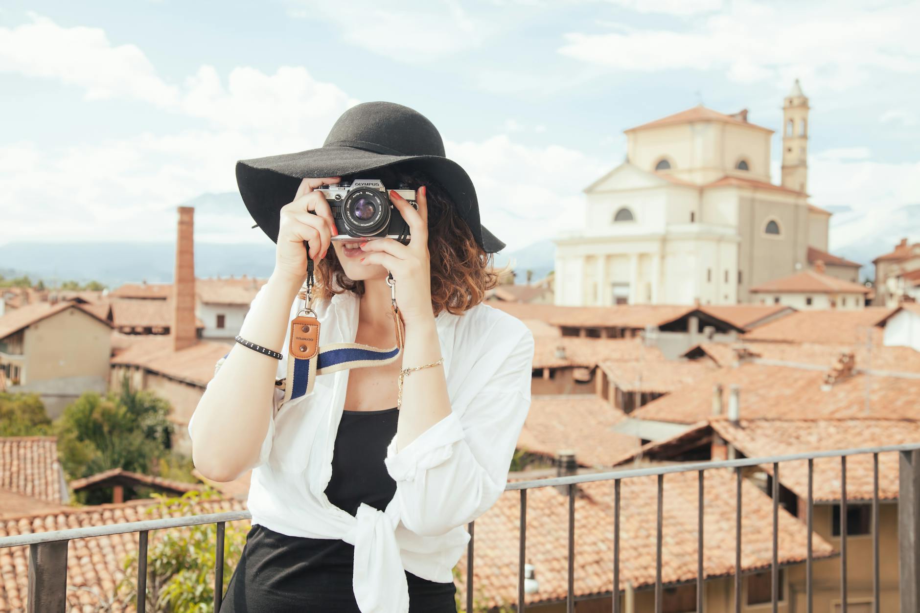 Woman with camera photographing European rooftops, blending fashion and travel imagery.
