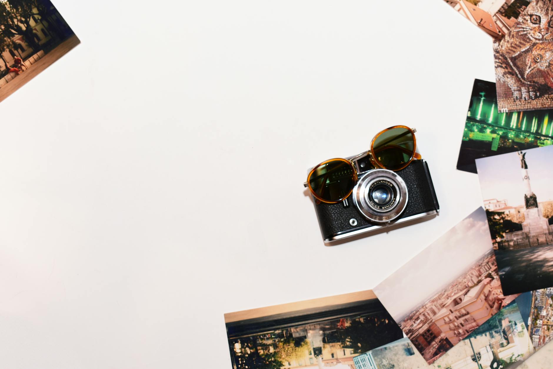 Top view of a vintage camera and sunglasses surrounded by travel photos on a white background.