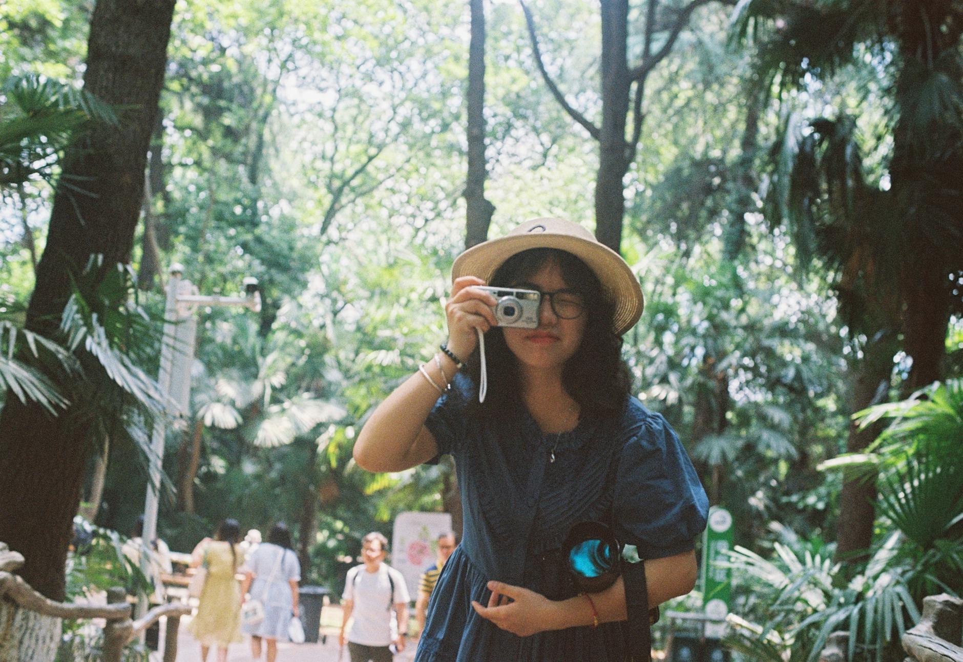 Asian woman taking photos in a lush green forest, capturing nature.