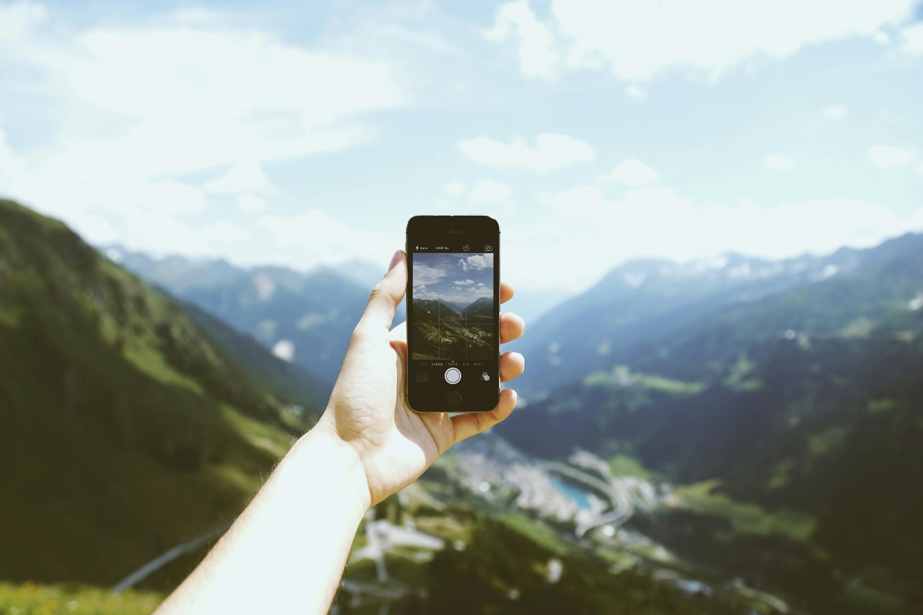 A hand holding a smartphone capturing a scenic mountain view under a clear sky.
