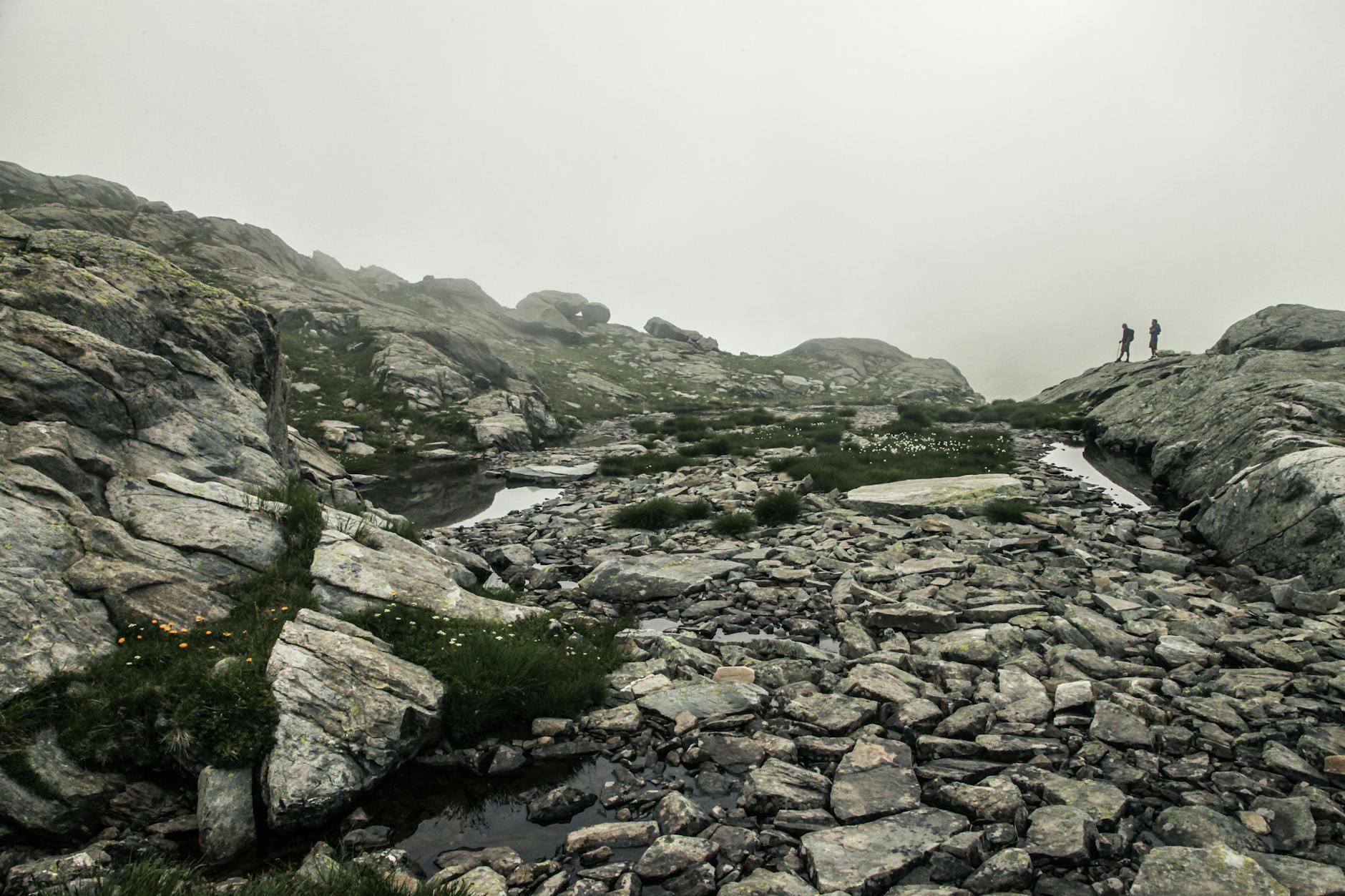 Two hikers exploring foggy rocky mountainside, exuding tranquility and adventure.