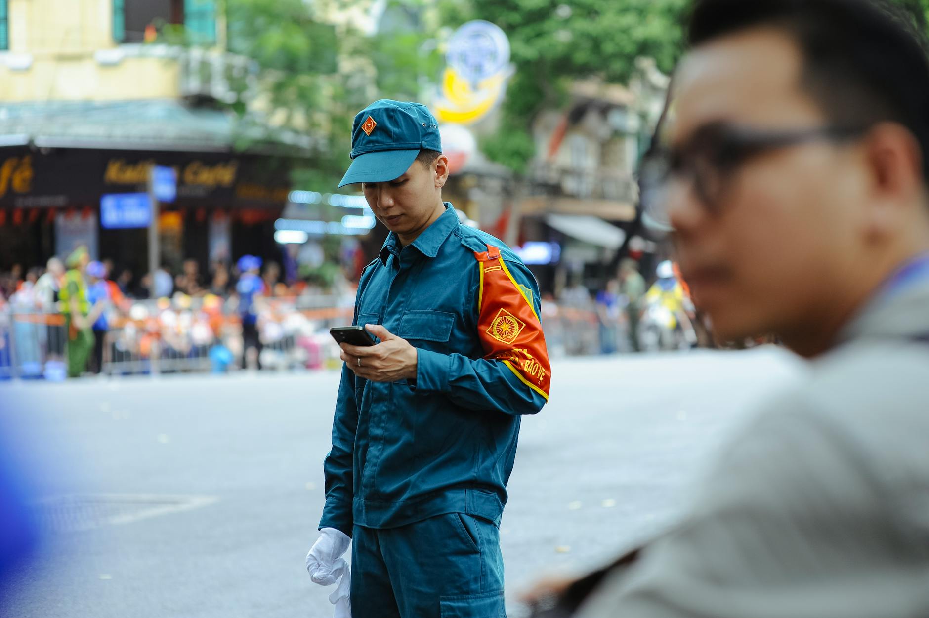 A Vietnamese officer in uniform looks at a smartphone while standing on a street in Hanoi.