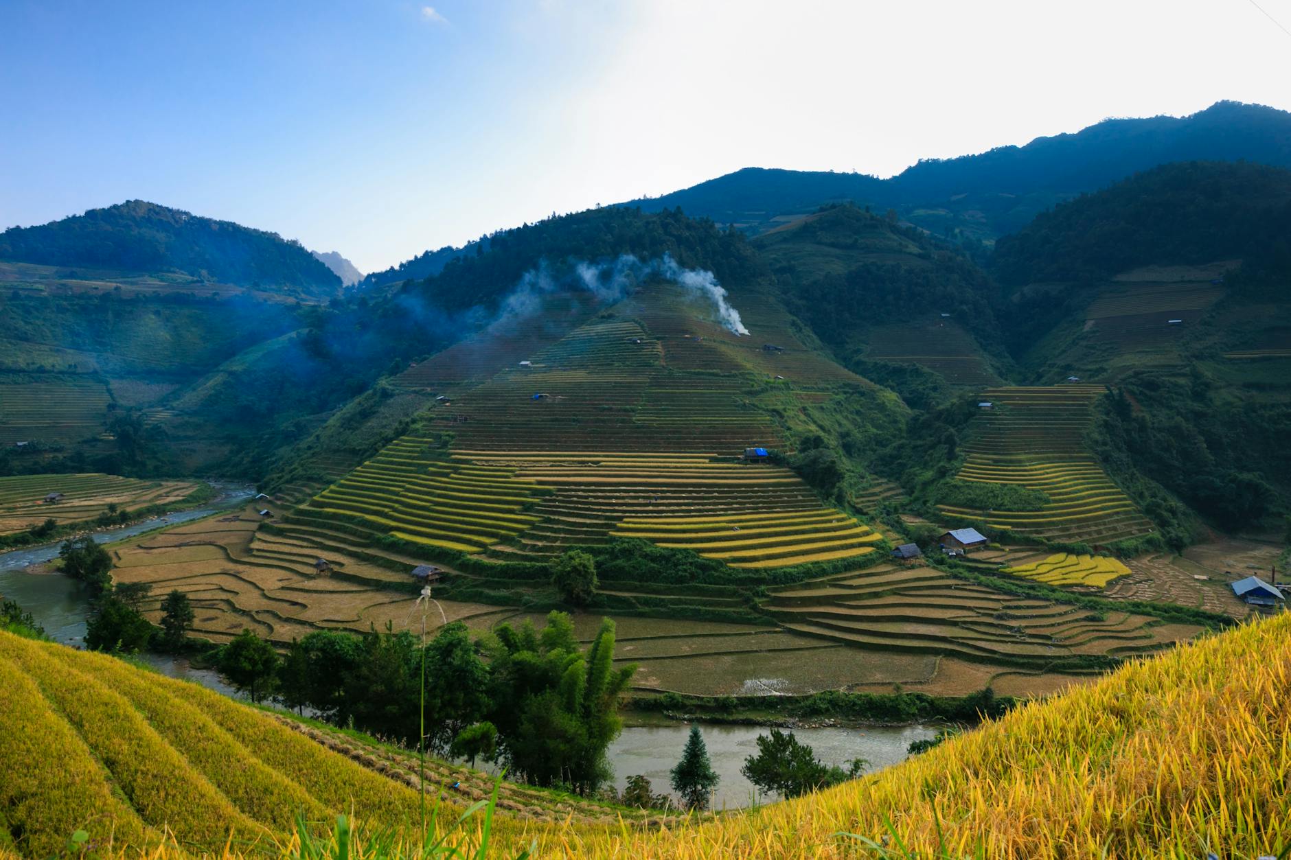 Lush green rice terraces covering hills under a blue summer sky, showcasing rural beauty.
