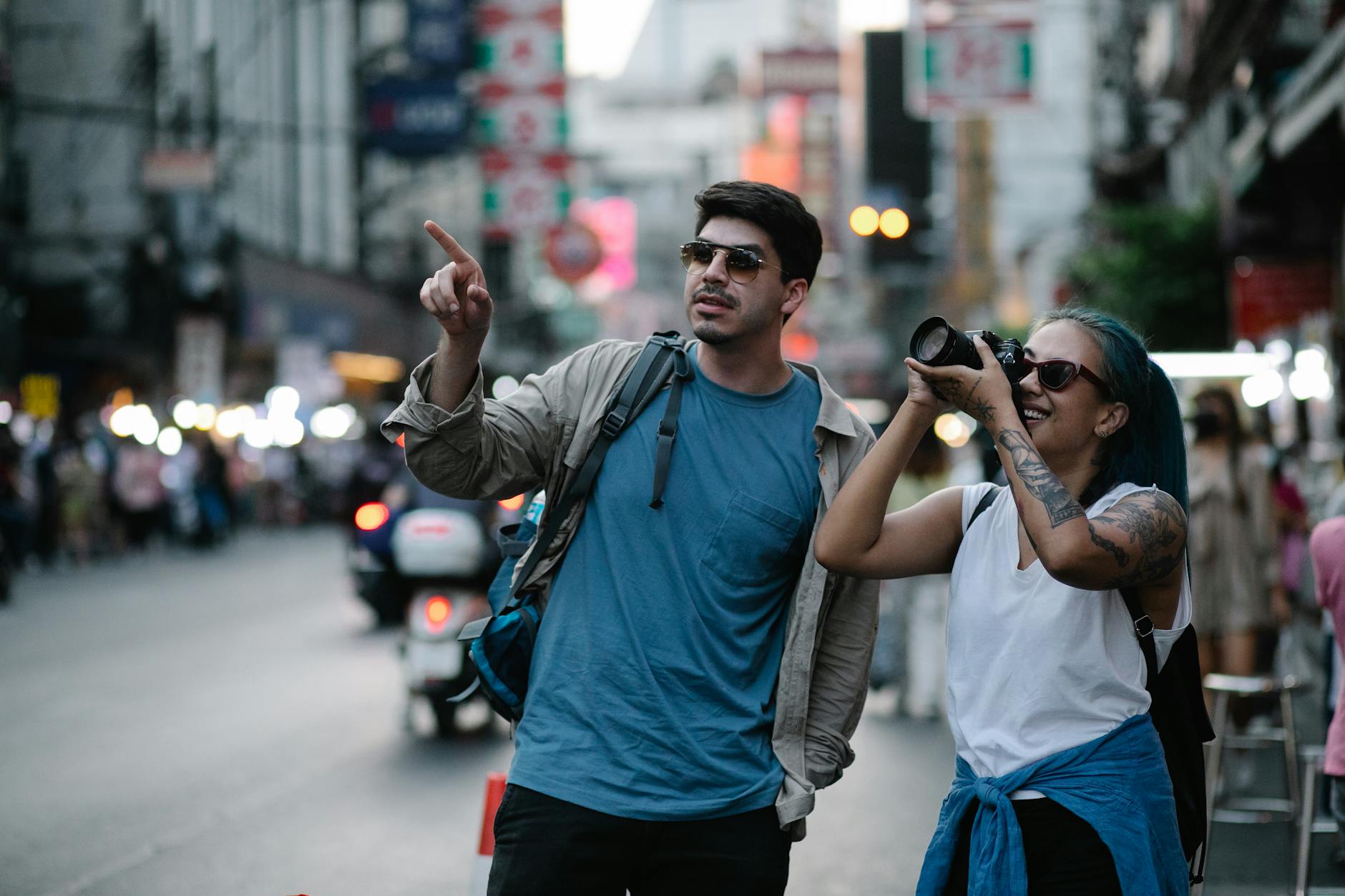 Two tourists capturing street scenes in a busy city, enjoying travel moments.