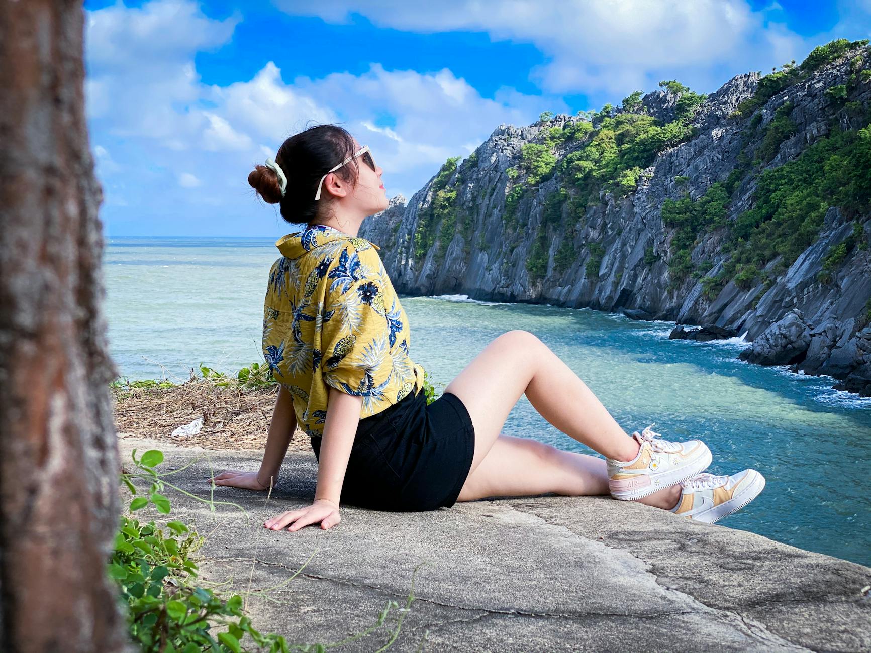 Young woman in sunglasses enjoys a cliffside ocean view in Vietnam under blue skies.