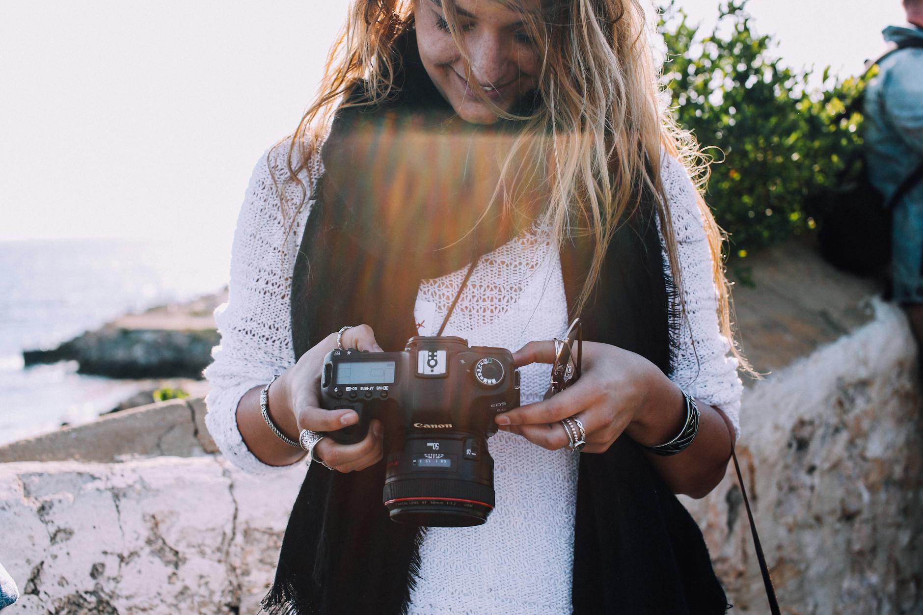 Content young female traveler checking pictures on photo camera while spending holidays at seaside