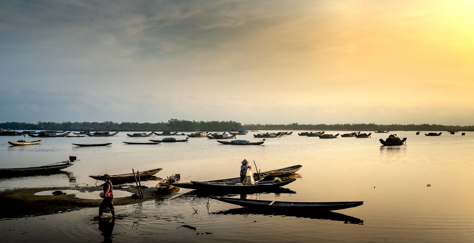 Fishermen prepare their boats at sunrise on a tranquil lake, reflecting the sky.
