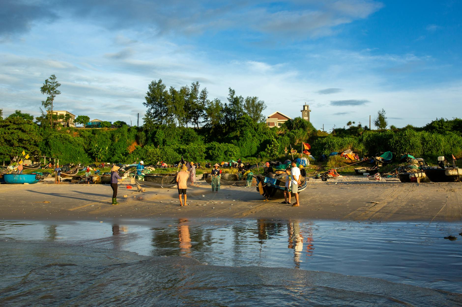 Fishermen working on a sunny beach with green hills and blue sky in the background.