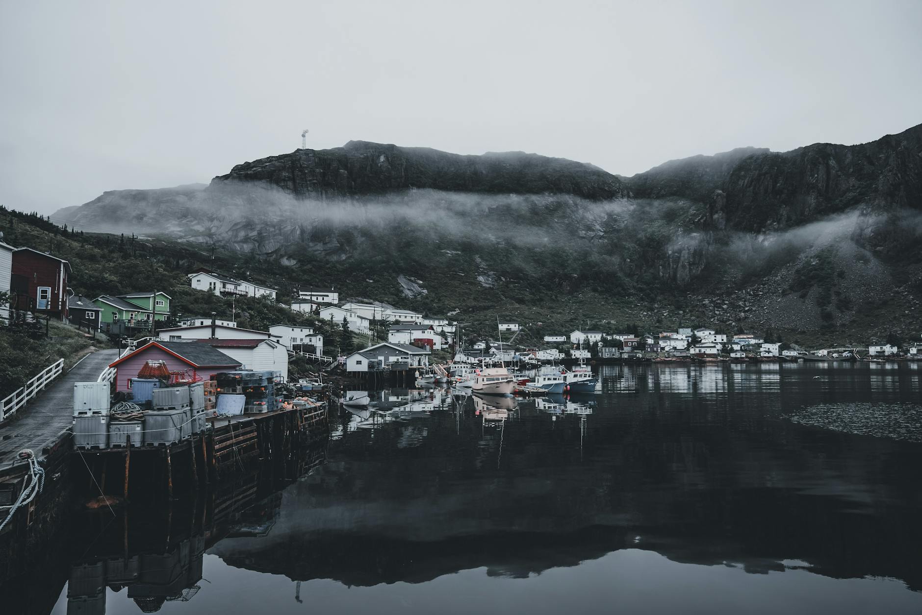 Scenic fishing village with mist-covered hills and calm harbor reflections.
