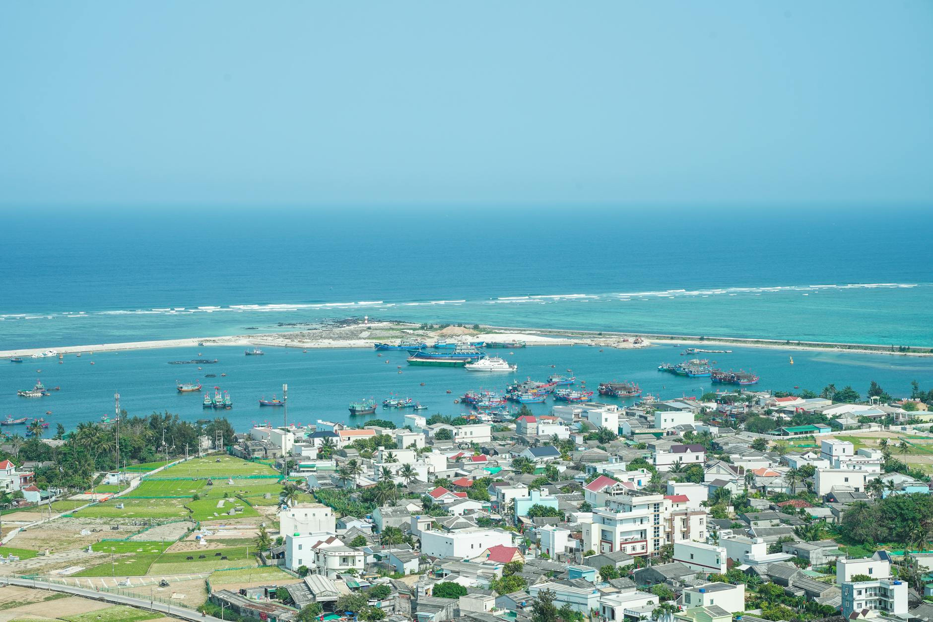 Aerial view of Ly Son Island harbor with boats and vibrant buildings, showcasing the tranquil turquoise sea.