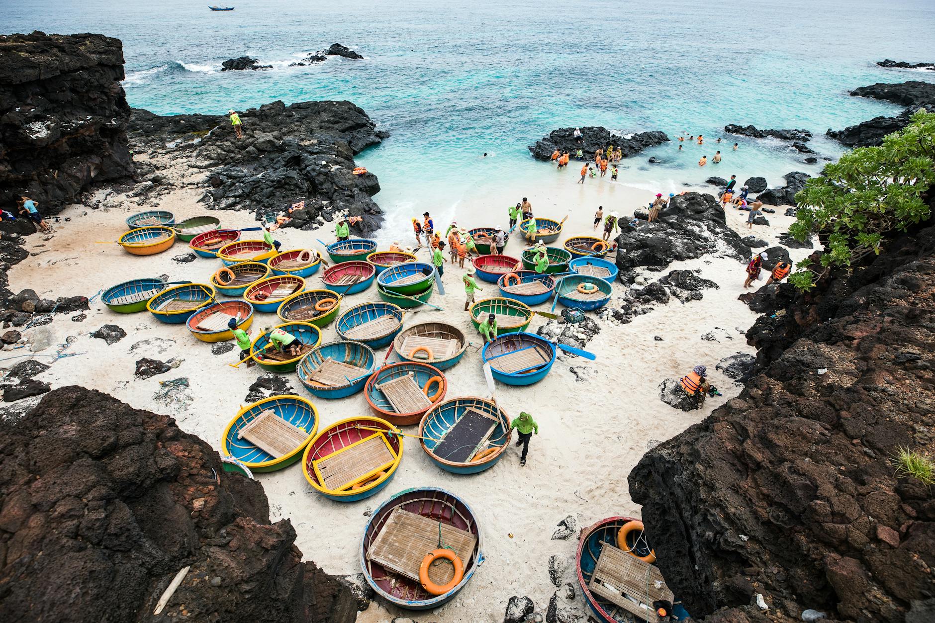 Aerial view of colorful basket boats by a rocky beach in Vietnam, with people enjoying the scene.
