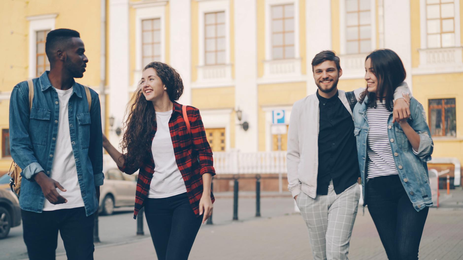 Group of four friends happily strolling through a city street on a sunny day.