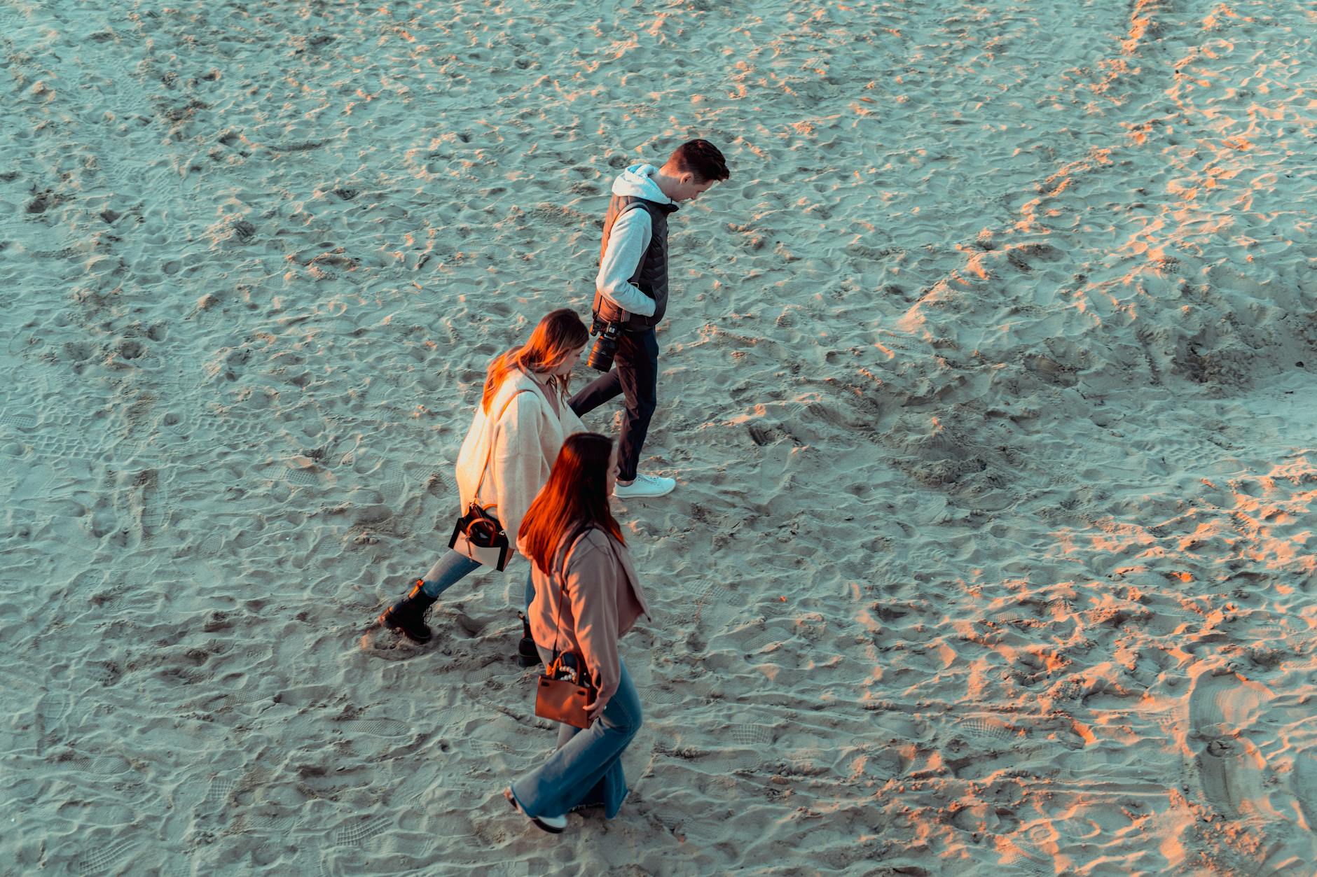 Aerial shot of three people walking on a sandy beach during daytime, enjoying outdoor leisure.