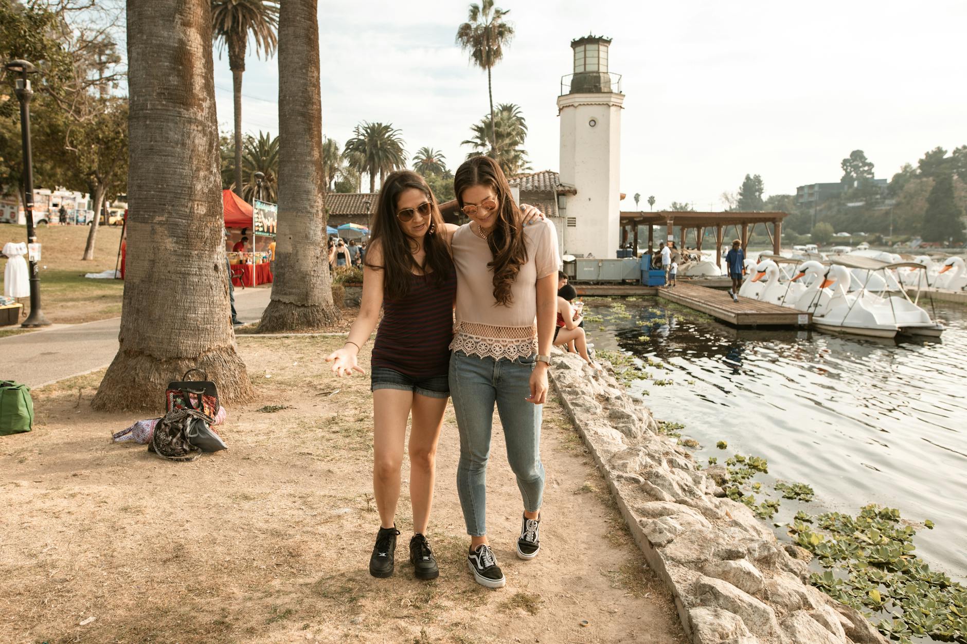 Two women enjoy a sunny walk by the lakeside, showcasing friendship and leisure.