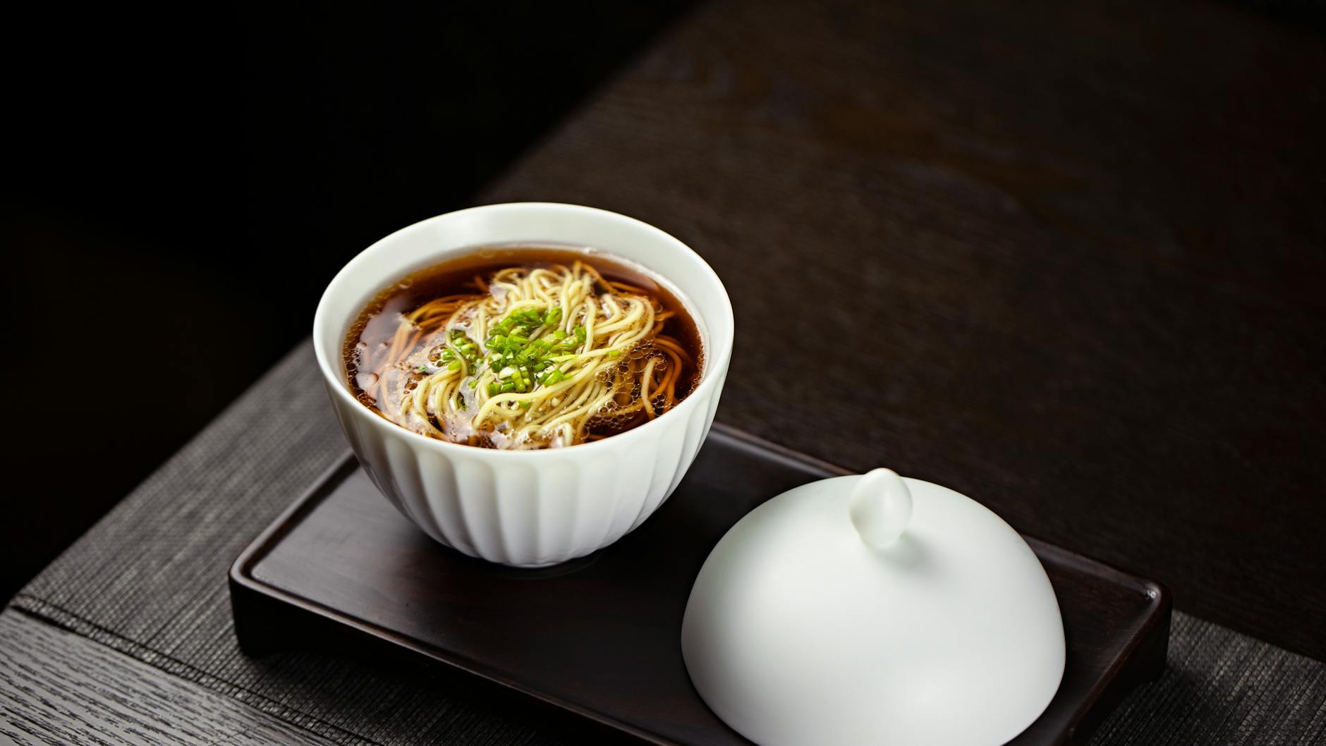 A close-up of a tasteful noodle soup garnished with greens, served in a bowl.