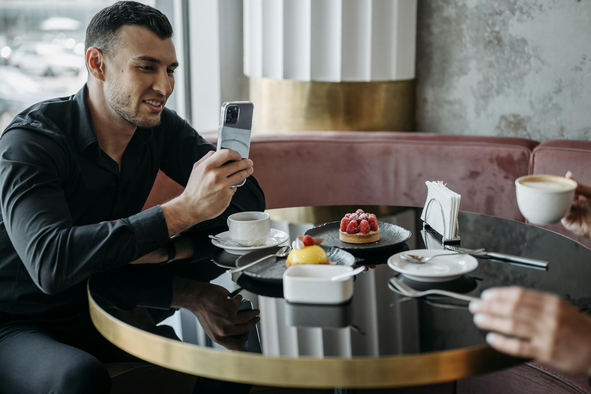 A man taking a photo of desserts at a modern café table while enjoying a coffee.