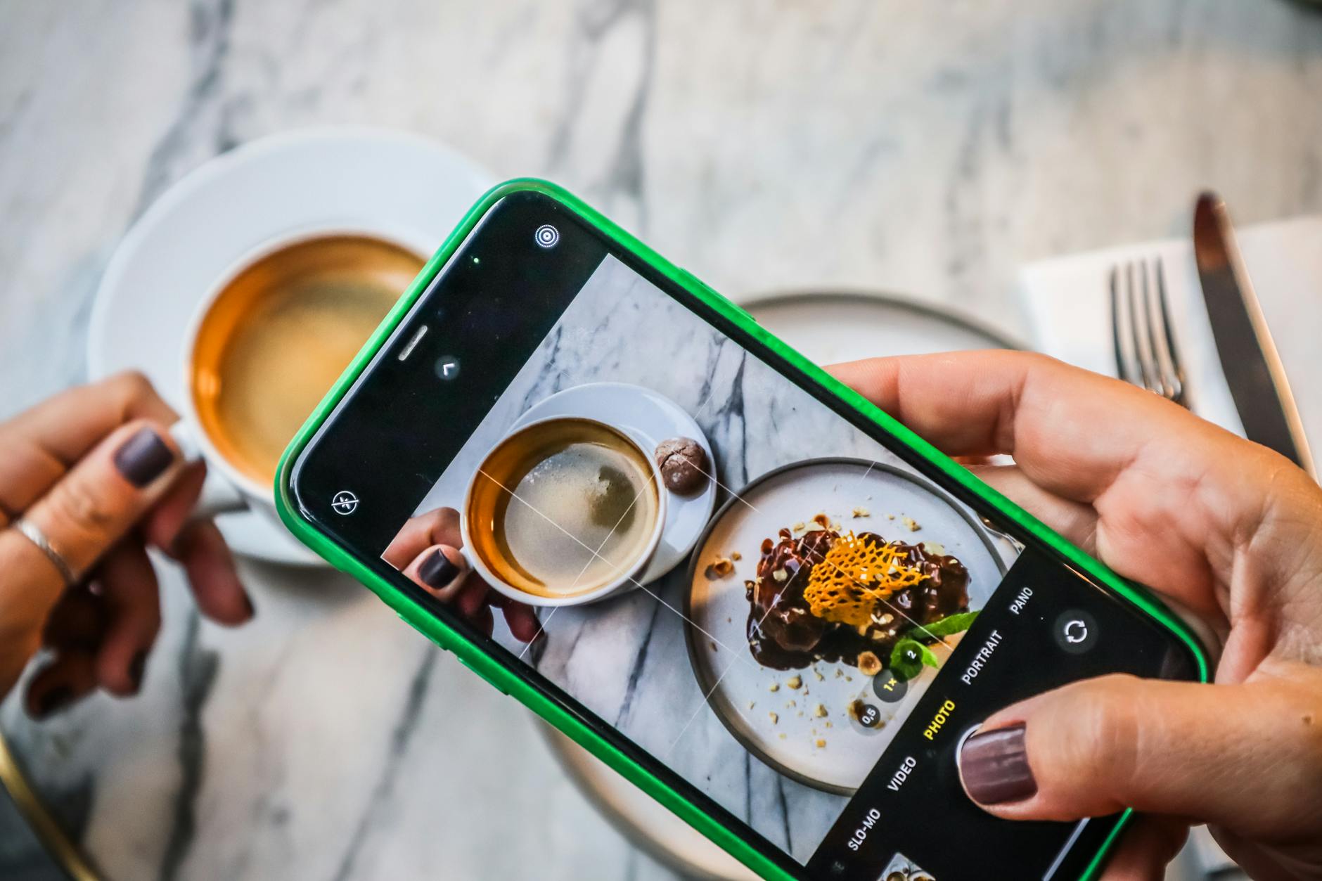A smartphone captures a delicious coffee and dessert moment in a cozy restaurant.