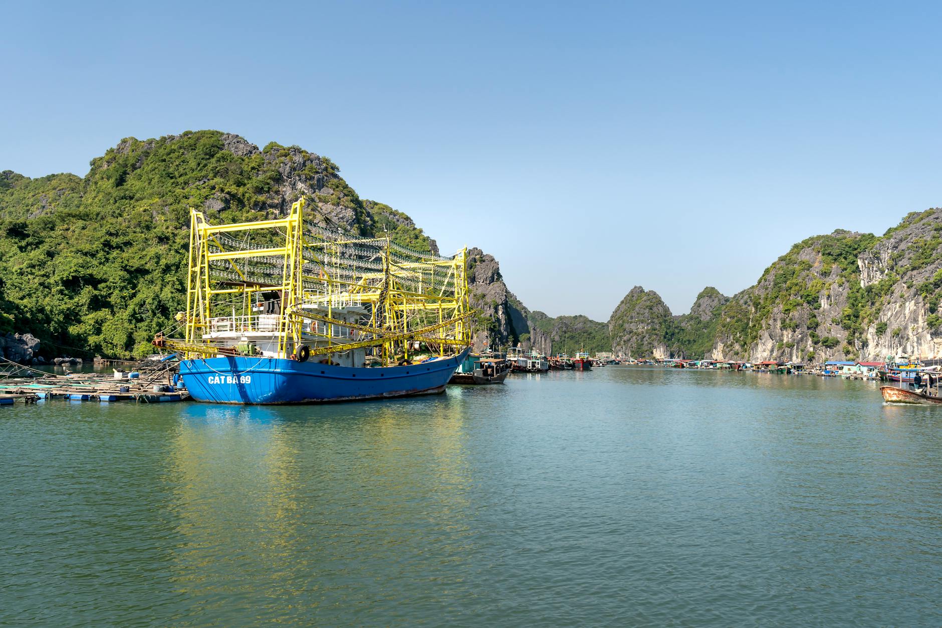 A vibrant fishing boat moored in a picturesque Vietnamese harbor, surrounded by lush hills.