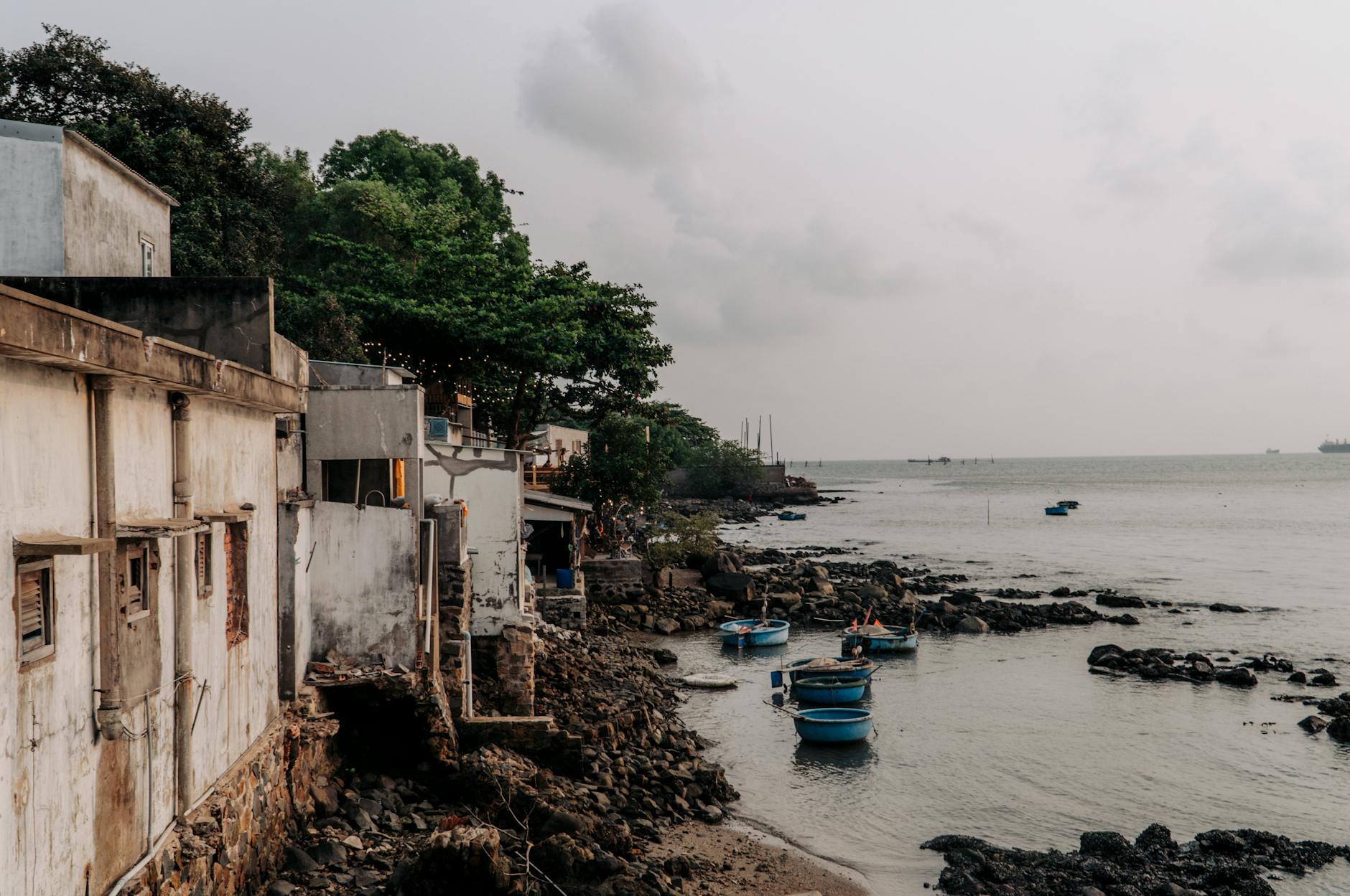 Rustic coastal village in Vũng Tàu, Vietnam, with old buildings and small fishing boats along the rocky shore.