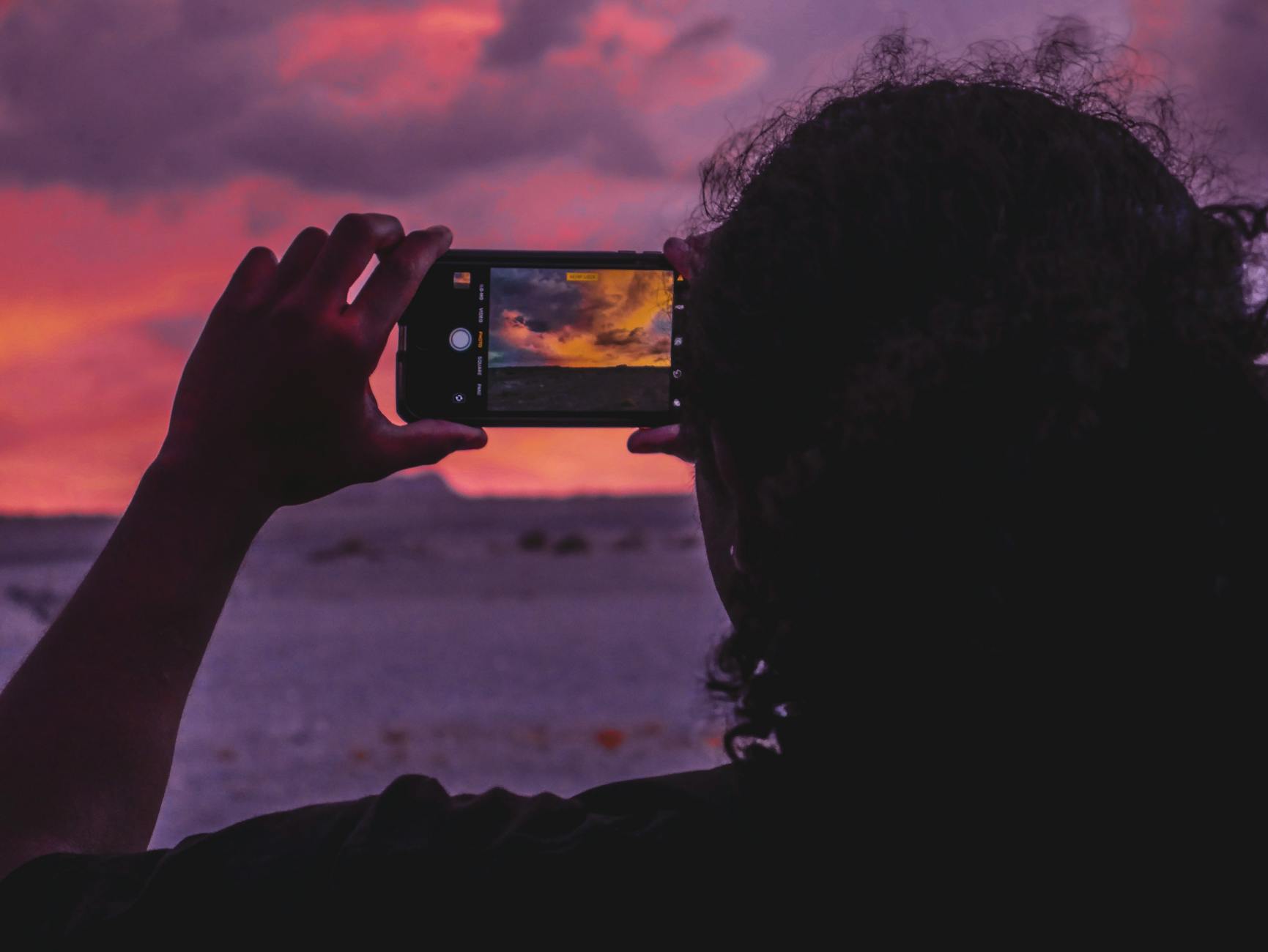 Silhouette of a person photographing a stunning sunset with a smartphone, creating an artistic frame.