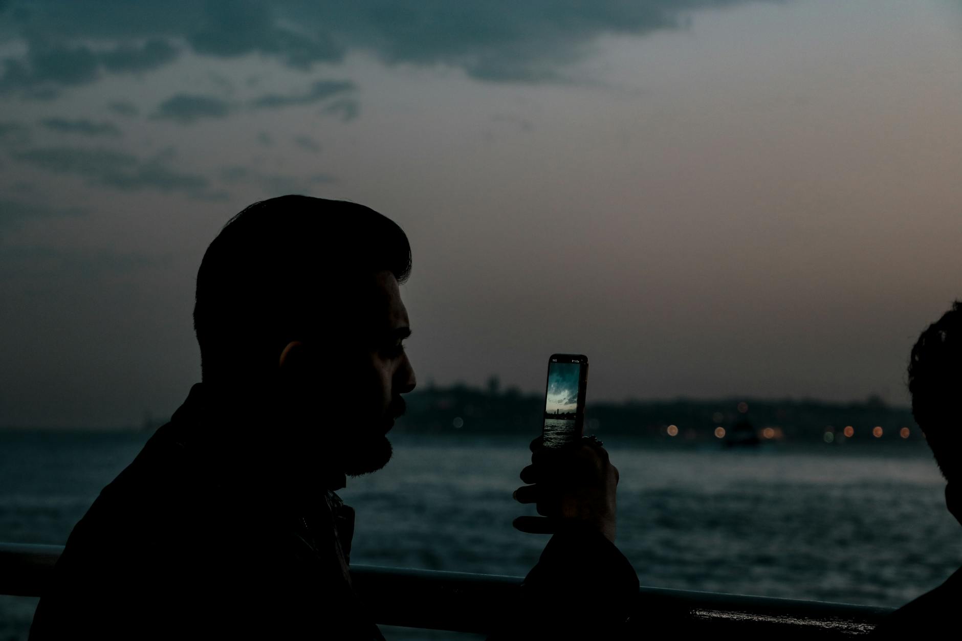A man silhouetted against the twilight sky takes a photo of Istanbul's waterfront.