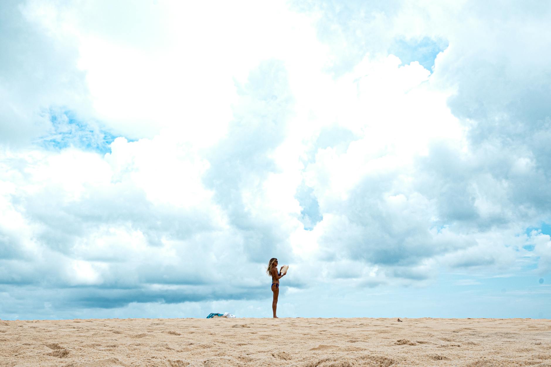 Solitary woman with mobile under a vast, cloudy sky on a beach in Natal, Brazil.