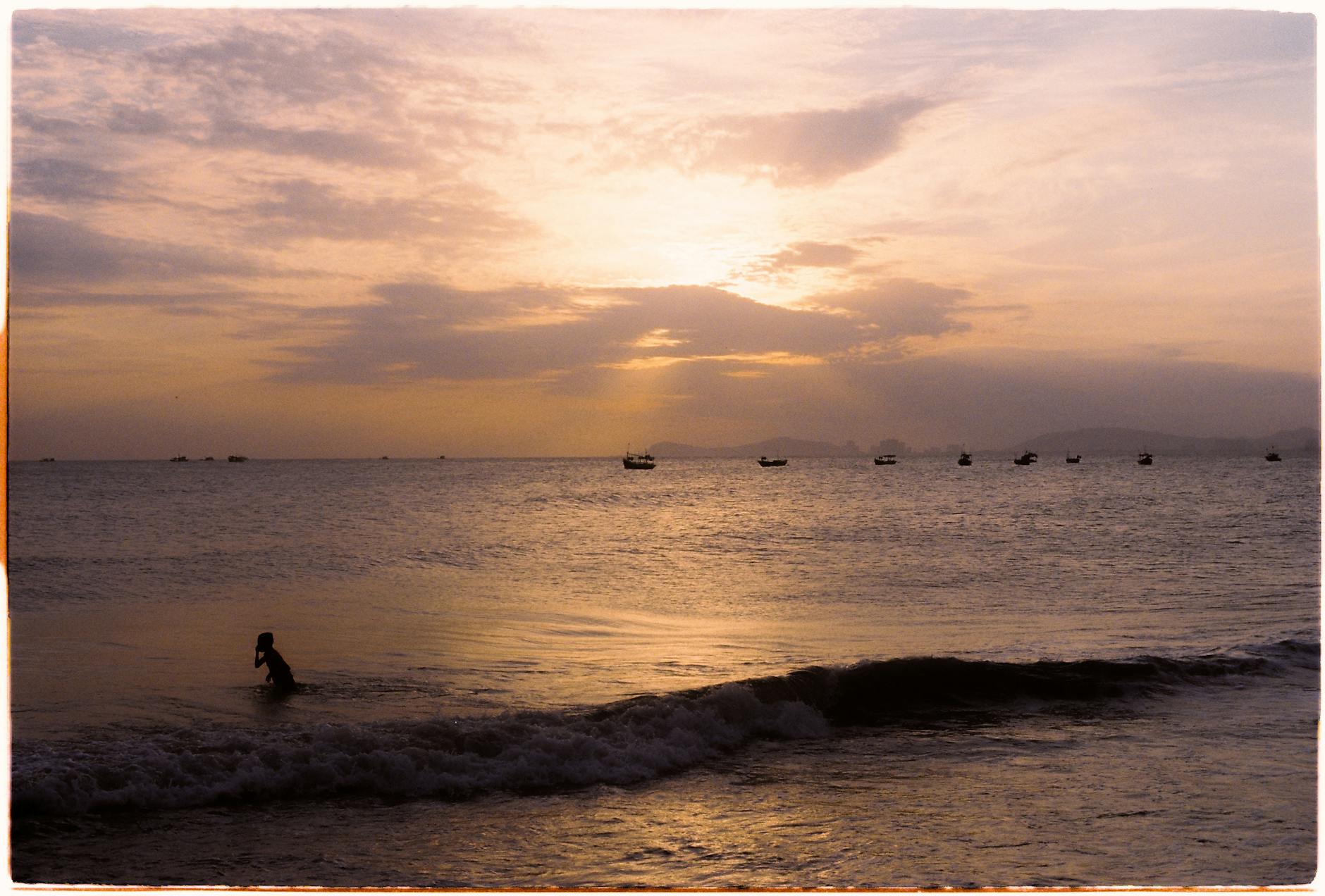 Serene view of a sunset over Vũng Tàu, Vietnam, featuring a lone silhouette and distant boats.