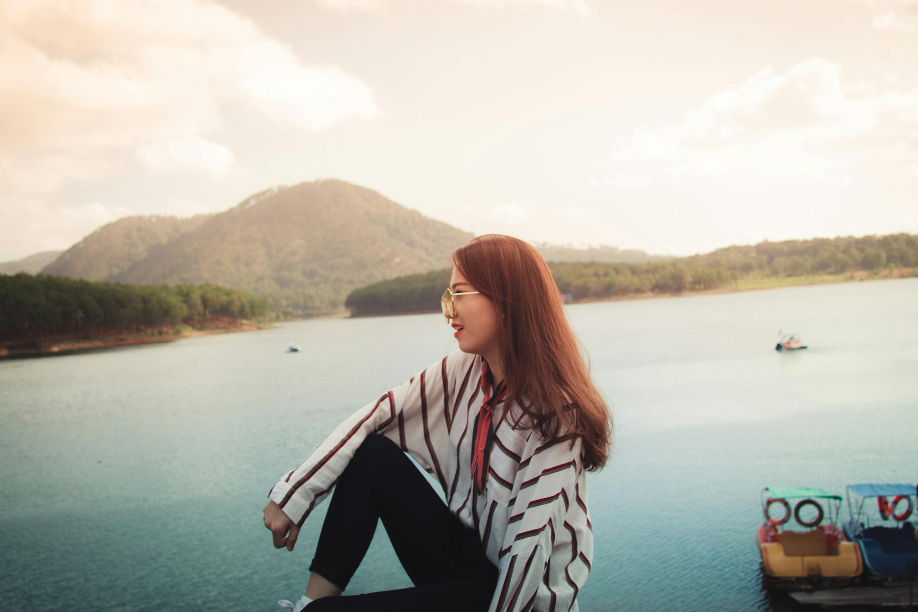 A woman in stylish attire enjoys the serene lake view in Da Lat, Vietnam, surrounded by mountains.