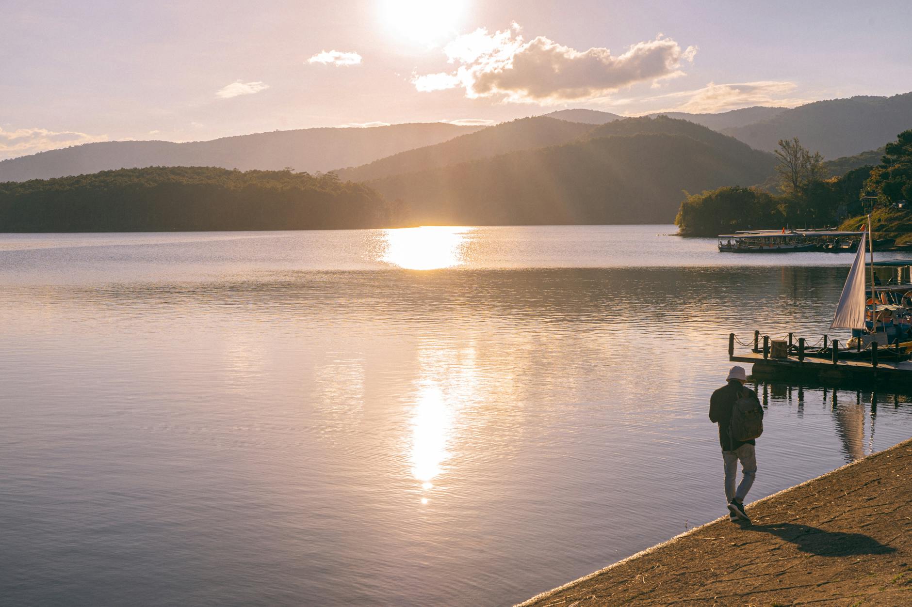A serene sunset at a tranquil lake in Da Lat, Vietnam with a silhouette walking by.