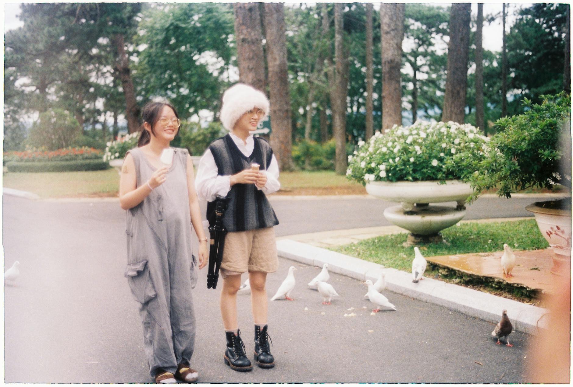 Two young adults enjoying a stroll among pigeons in a lush Đà Lạt park.