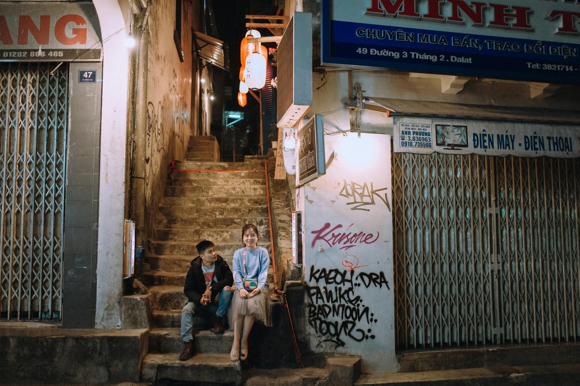 A young couple enjoying a quiet moment in a graffiti-lined urban alley at night.