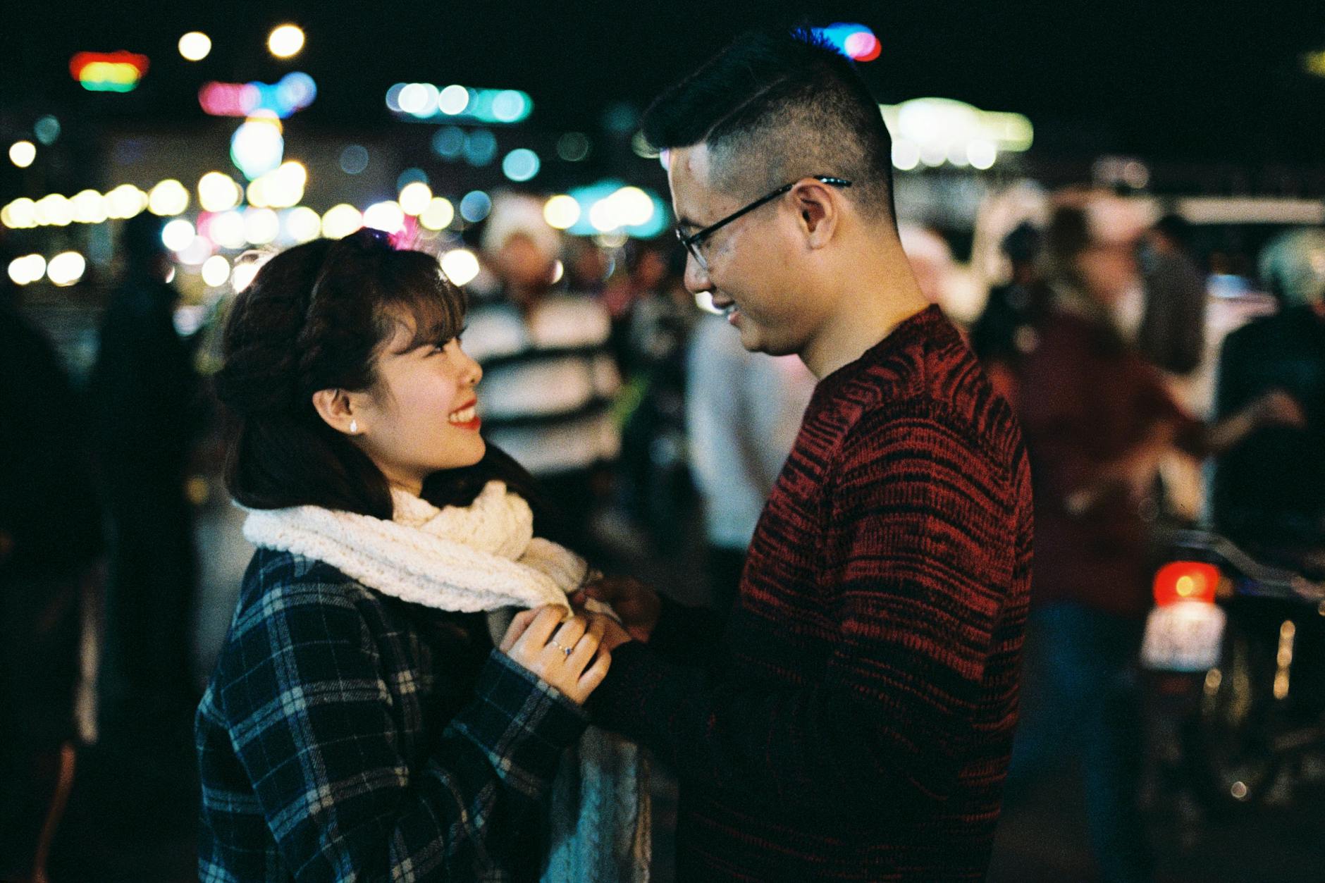A couple enjoys a warm moment amidst the lively streets of Dalat, Vietnam at night.