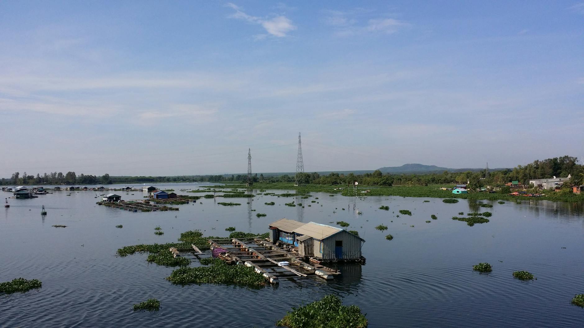 Floating houses on Mekong River with lush vegetation and clear sky in Vietnam.