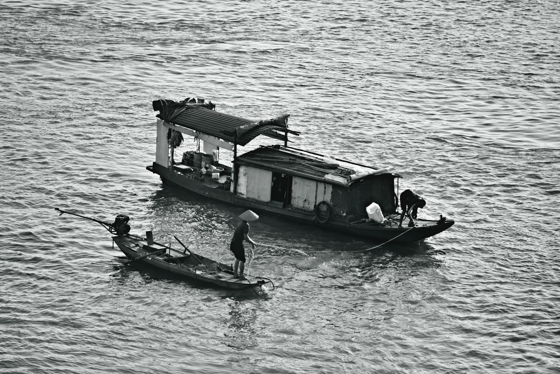 Black and white image of traditional fishing boats with people on a calm river.