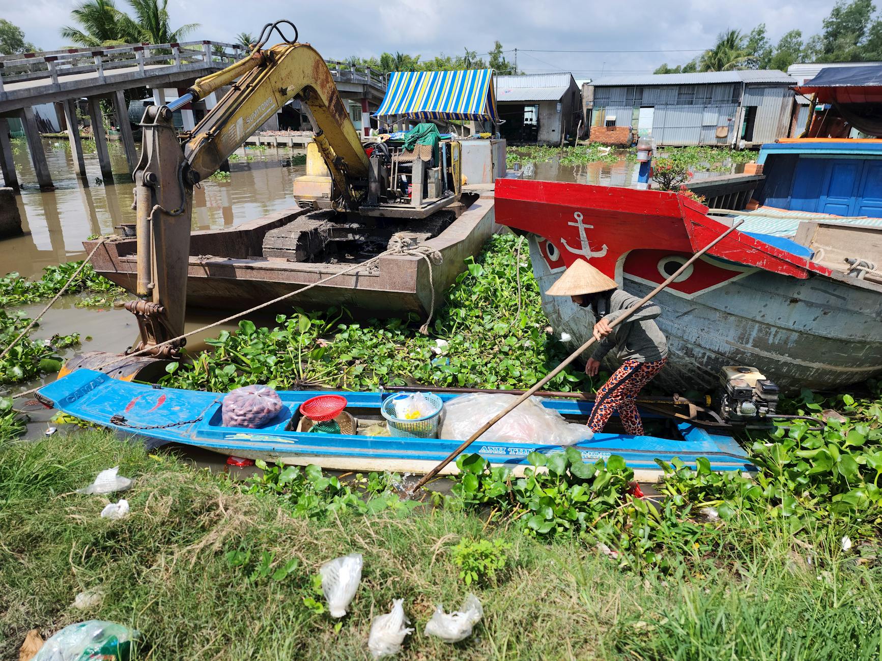 A vibrant scene of a traditional boat and excavator on a river in Phụng Hiệp, Vietnam.