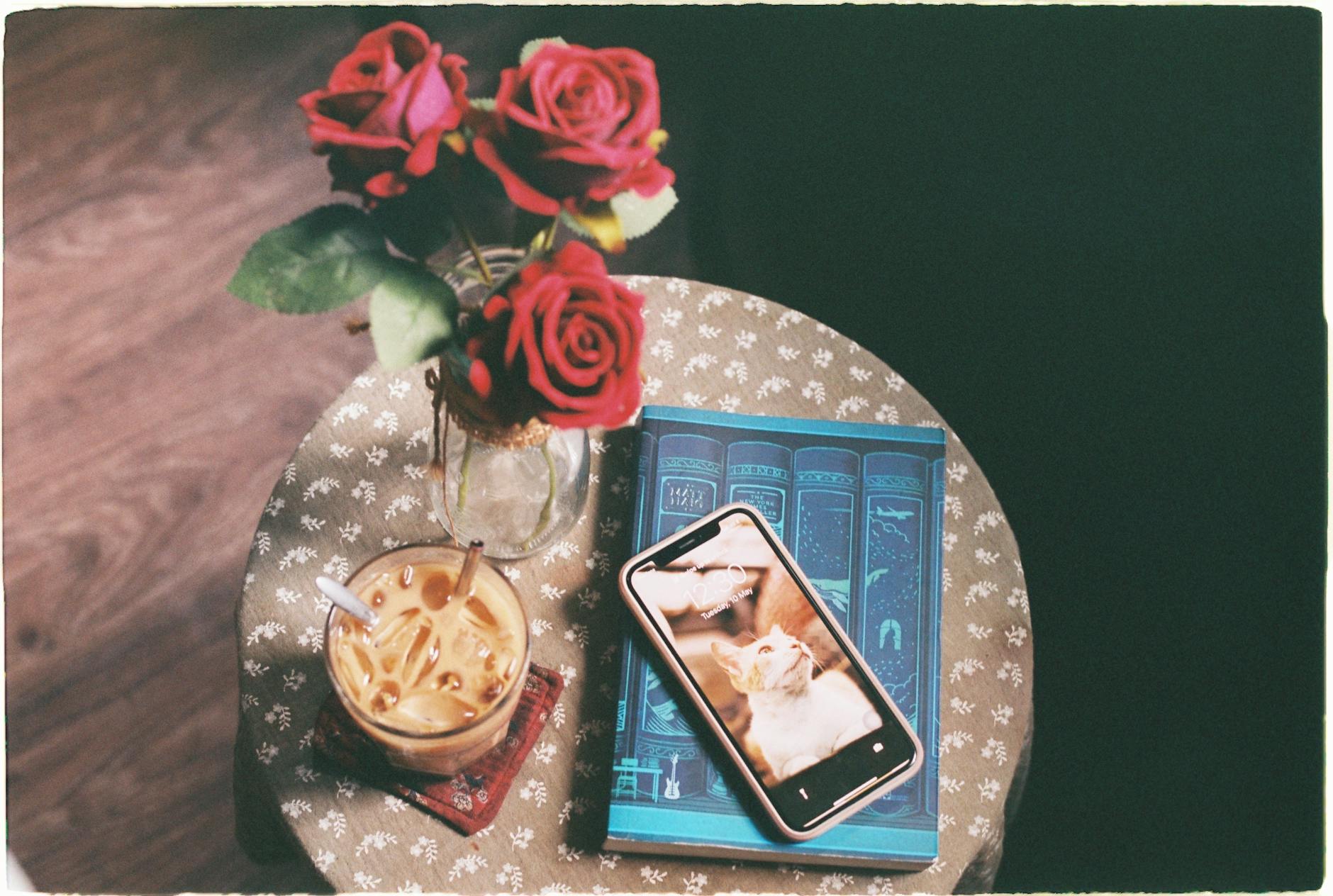 Aesthetic composition with roses, iced coffee, and smartphone on a vintage table.
