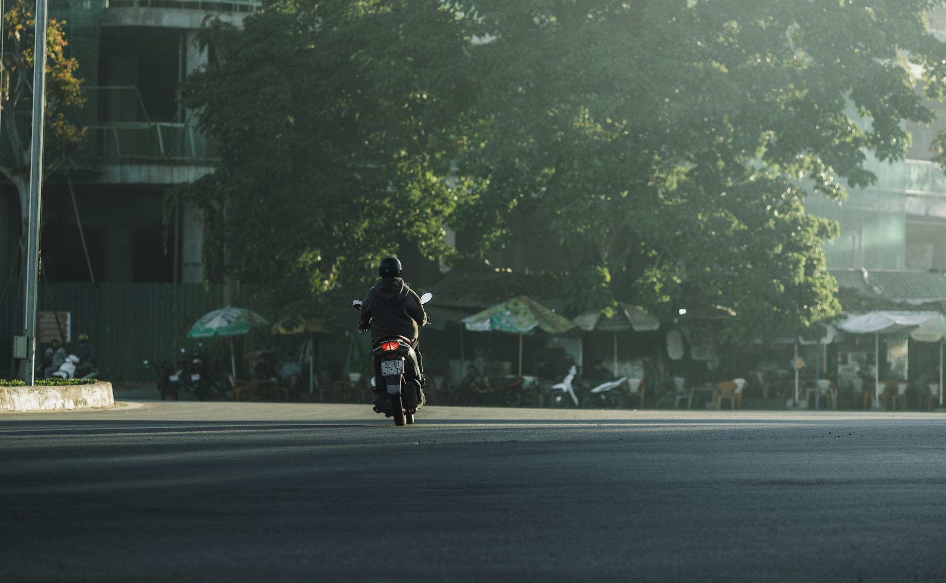 A person on a motorcycle drives through a quiet street in Kon Tum, Vietnam, during early morning light.