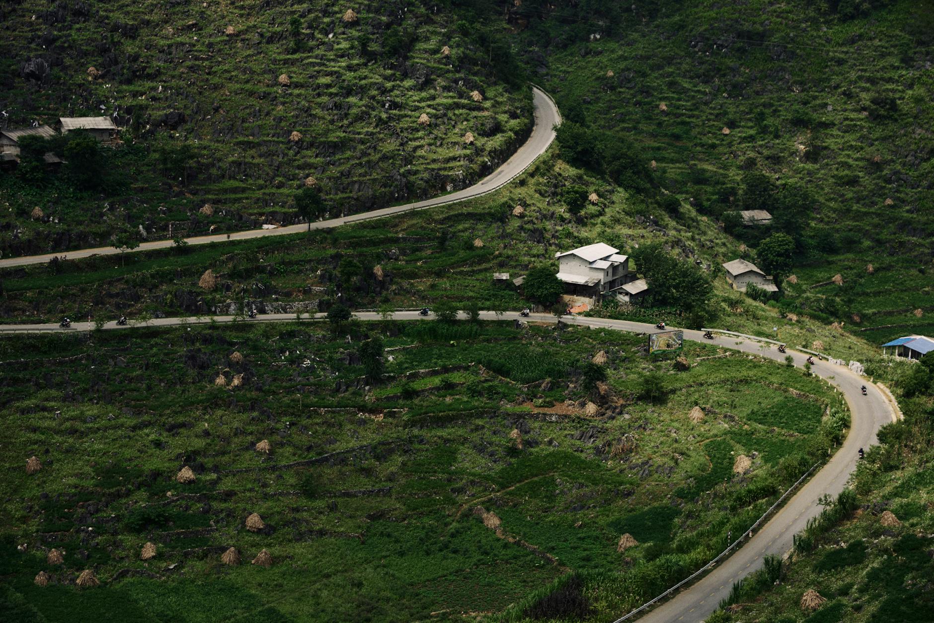 A winding mountain road in lush green terrain of Hà Giang, Vietnam, showcasing rural landscapes.