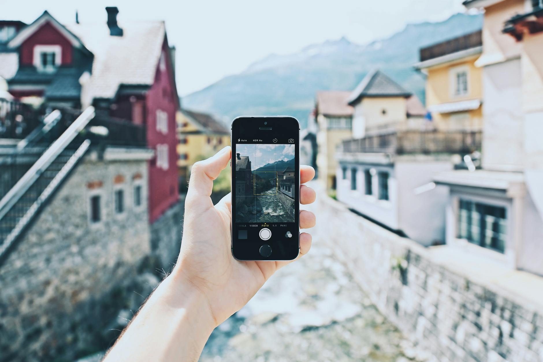 A hand holding a smartphone capturing a scenic mountain village view.