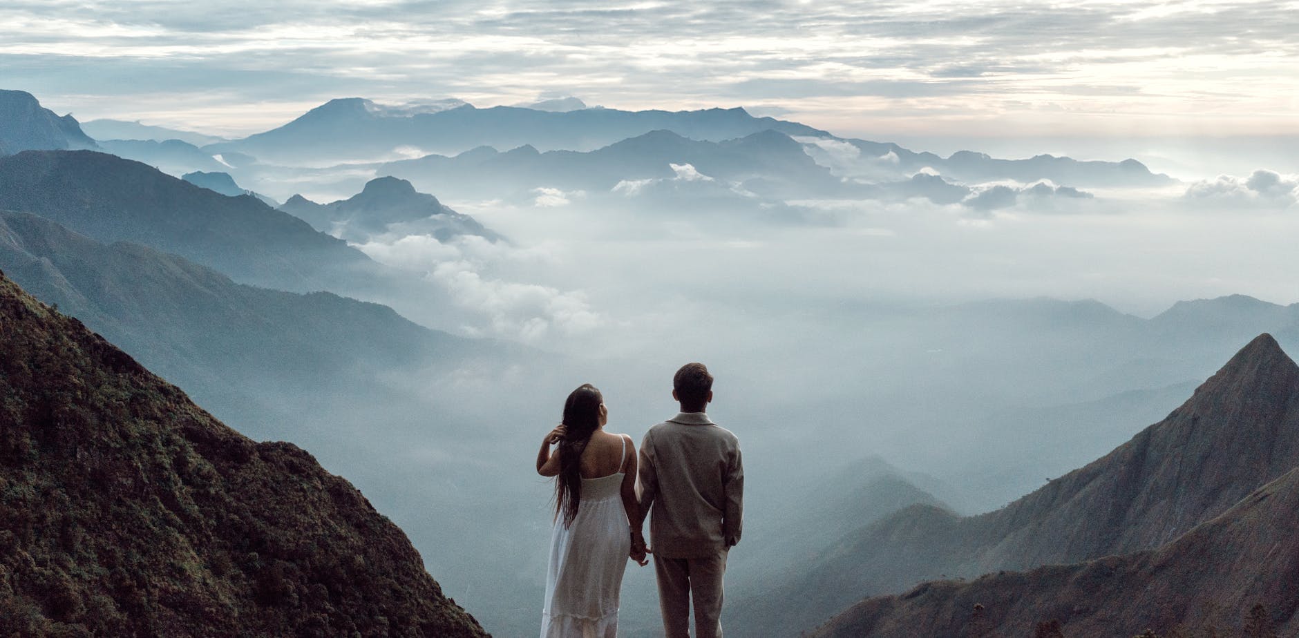 A couple stands hand in hand marveling at the breathtaking Munnar mountain landscape.