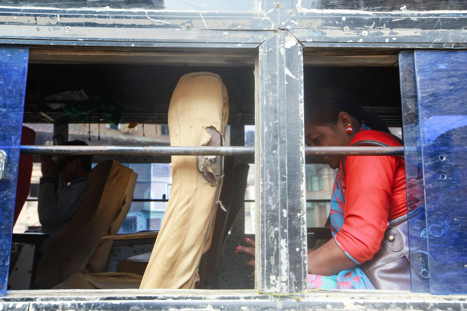 A woman sits inside a dilapidated bus, engrossed in her phone, showcasing vibrant traditional clothing.