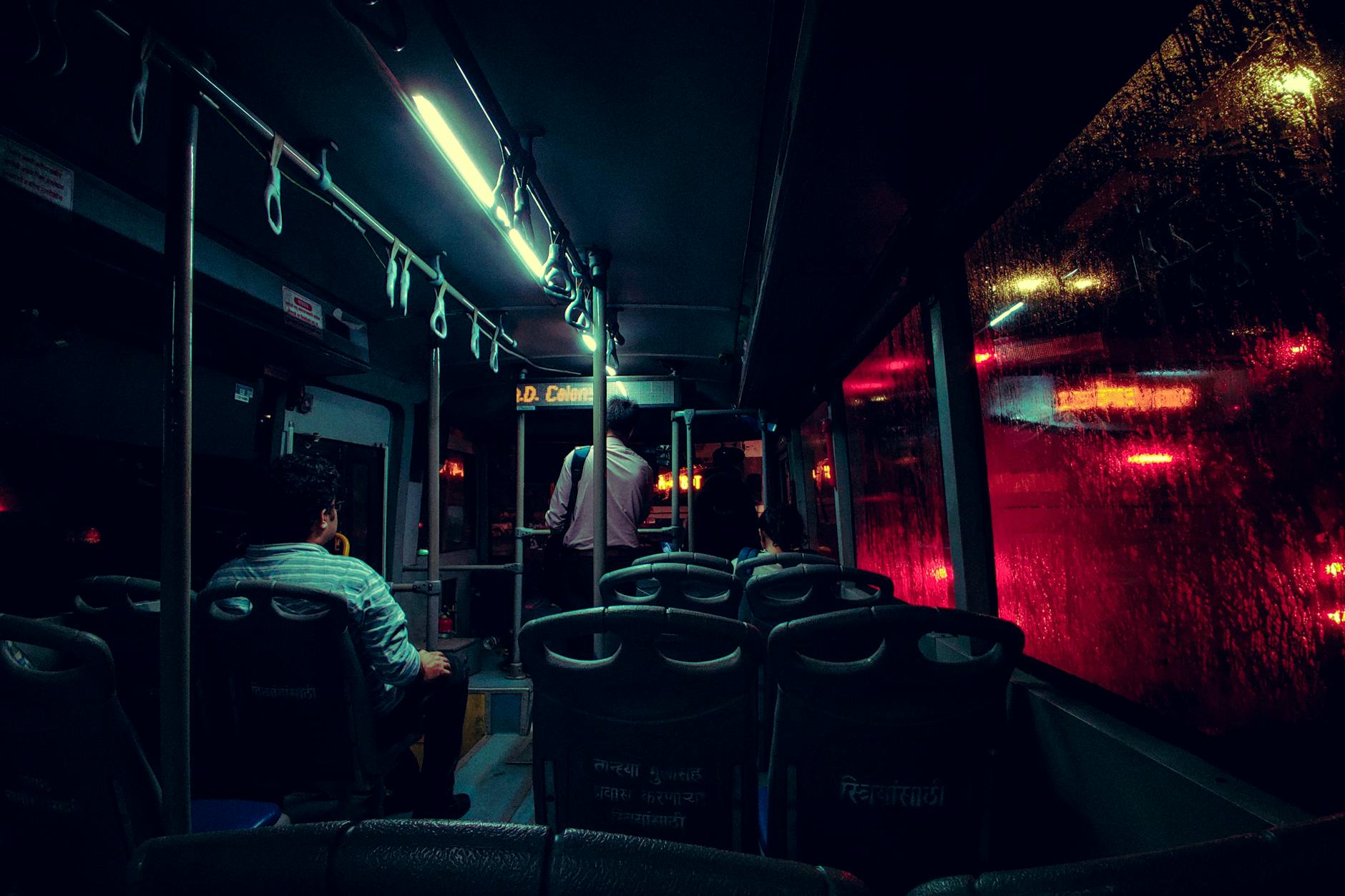 Inside view of a dimly lit bus with passengers during a rainy night in Mumbai, India.